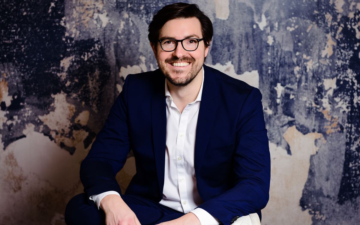 Christian Wenzel sitting and smiling in front of a wall